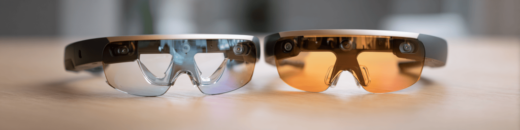 Panoramic close-up of two Microsoft HoloLens 2 AR headsets with clear and amber lenses, representing advanced mixed reality and spatial computing technology.