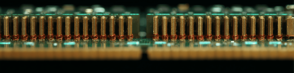 Panoramic macro shot of neat gold-plated connector pins with red winding wires on PCB circuit board, representing precise electronic hardware connection and semiconductor manufacturing technology.