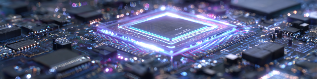 Wide panoramic macro shot of a core CPU chip ringed by glowing purple-blue neon light, set atop a densely populated printed circuit board dotted with colorful bokeh lights for advanced computing hardware.